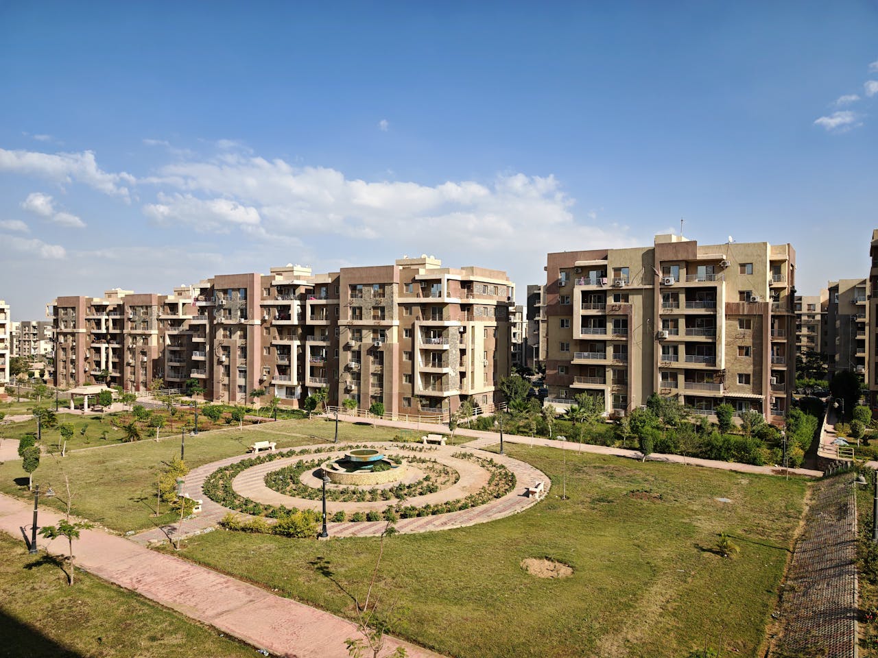 Modern apartment buildings with central landscaped garden under a clear blue sky.