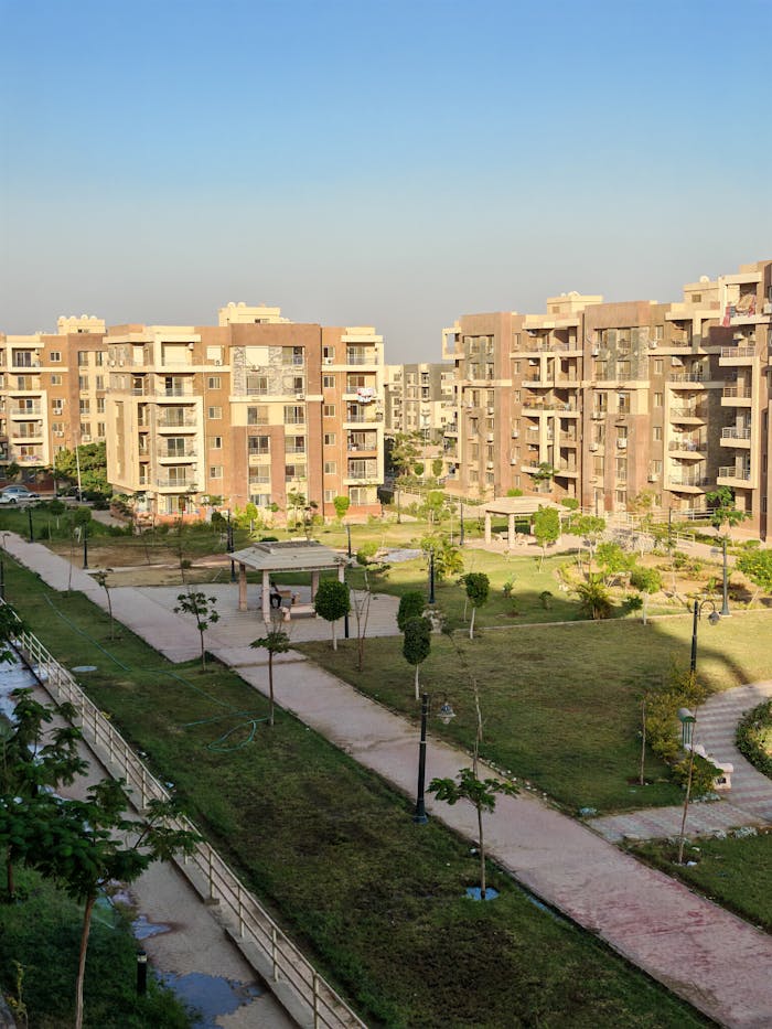 A scenic view of a modern residential complex surrounded by greenery under a clear blue sky.
